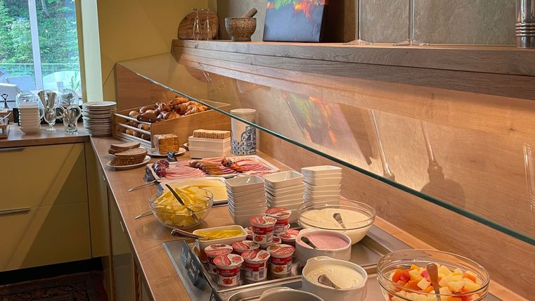Ein reichhaltiges Frühstücksbuffet mit frischen Früchten, Joghurt, verschiedenen Aufschnittarten und Brötchen. Die Präsentation ist hell und einladend.