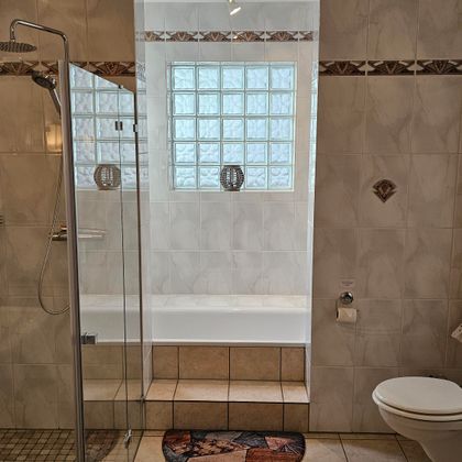 A modern bathroom with a shower and a bathtub. The walls are light tiled and there is natural lighting from a window.