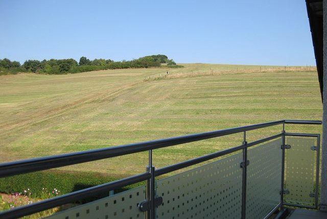 A balcony overlooking a vast green field under a clear blue sky. The lawn features even cutting patterns and gentle hills.