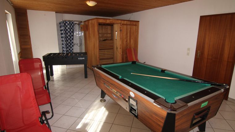 Ein Freizeitbereich mit einem Billardtisch und zwei roten Stühlen. Im Hintergrund befinden sich eine Sauna und ein Tischkicker.