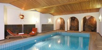 An elegant indoor pool with a wooden ceiling and warm light. Relaxed loungers invite you to linger.