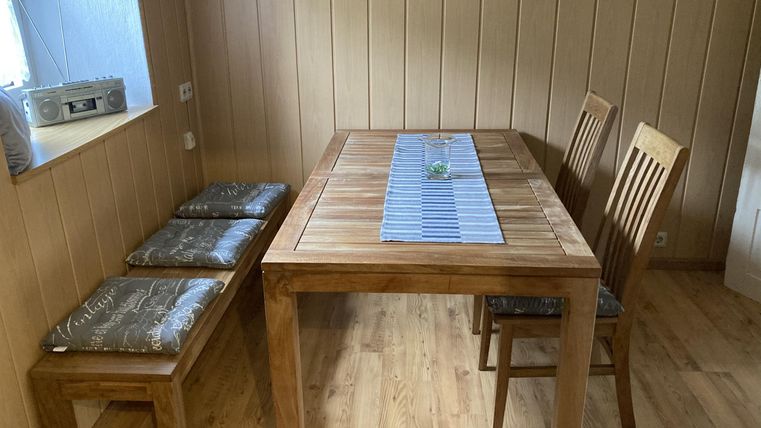 Een eenvoudige houten stoel en een tafel in een gezellige kamer. Een bank staat naast de tafel, en er ligt een blauwe loper op.