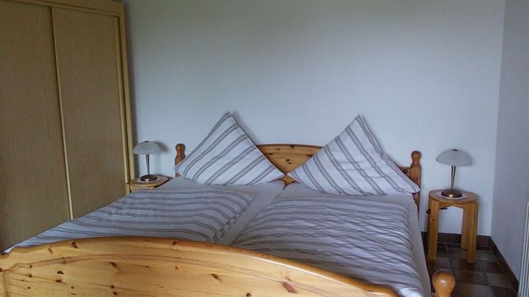 A cozy bedroom with a wooden bed and two pillows. Next to the bed are nightstands with lamps.