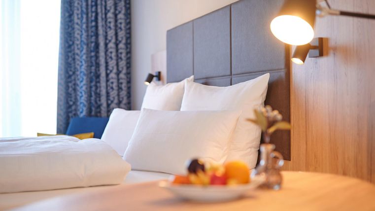 Ein modernes Schlafzimmer mit einem großen Bett und weißen Bettdecken. Auf dem Tisch steht eine Schale mit frischem Obst.