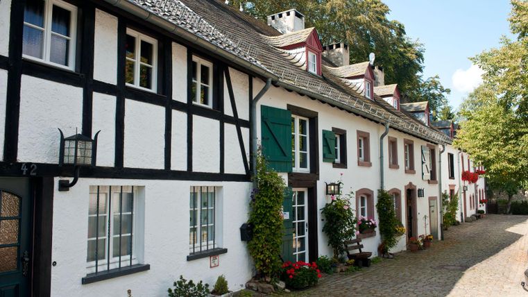 Eine malerische Straße mit historischen Fachwerkhäusern. Die Häuser sind von bunten Blumen und grünen Pflanzen umgeben.