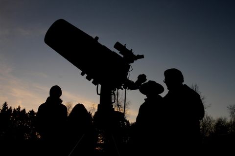 Eine Gruppe von Menschen beobachtet den Himmel durch ein teleskop. Sie stehen im Gegenlicht während der Dämmerung.