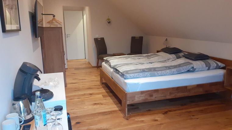 Ein schlichtes, modernes Zimmer mit einem Doppelbett und Holzfußboden. Am Tisch stehen Getränke und ein Fernseher.