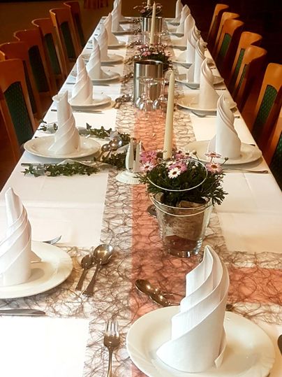 Ein festlich gedeckter Tisch mit eleganten Servietten und Dekoration. In der Mitte befinden sich Blumenarrangements und Kerzen.
