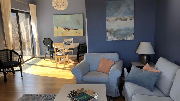 Een moderne woonkamer met een witte bank en een salontafel. De muren zijn geschilderd in een zachte blauwtint en er komt veel daglicht binnen door de ramen.