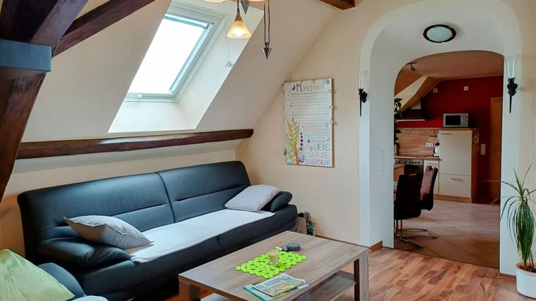 A bright living room with comfortable sofas and a large window. The room has a modern, inviting style with light wooden floors.