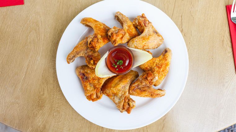 A plate with crispy chicken wings, surrounded by a portion of ketchup. The plate is arranged on a wooden table.