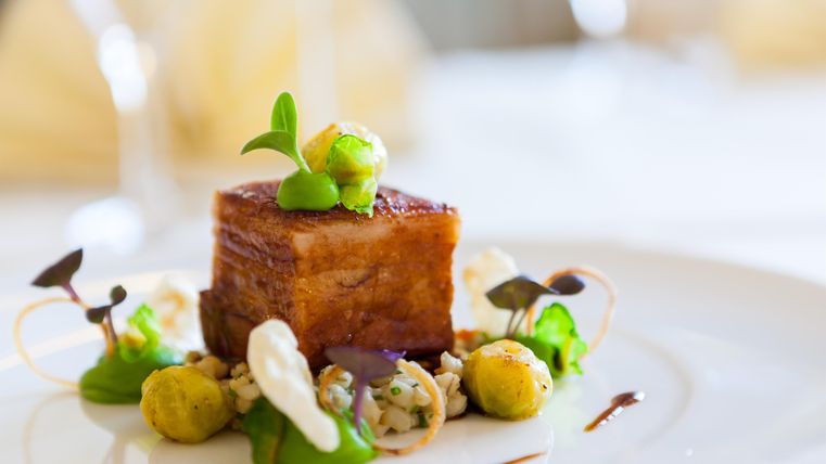 Ein kunstvoll angerichtetes Gericht mit gegrilltem Fleisch, frischem Gemüse und einer dekorativen Soße. Die Präsentation ist elegant und ansprechend.