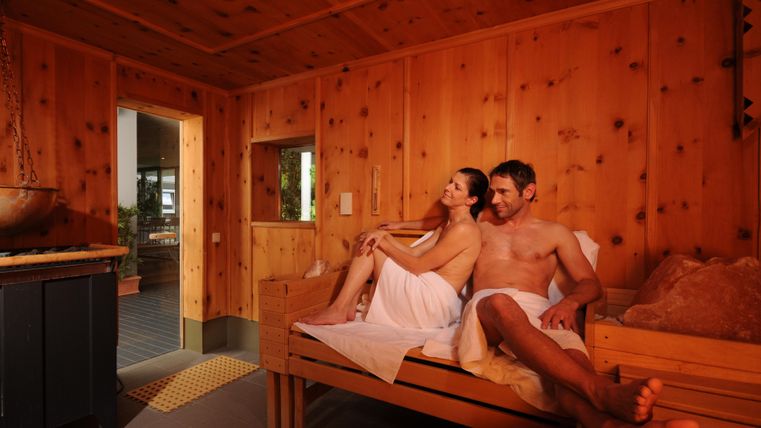 Een stel ontspant in een houten sauna-ruimte. De sfeer is gezellig en uitnodigend.