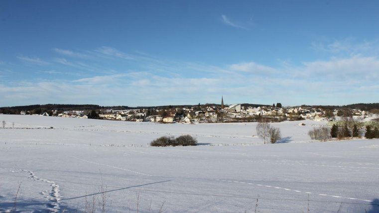 Eine verschneite Landschaft mit einem kleinen Dorf im Hintergrund. Der Himmel ist klar und blau.