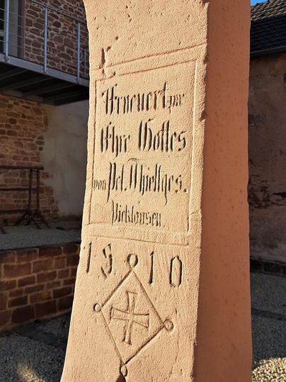 Een historische steen met een inscriptie die een monument eert. Het jaar 1910 is duidelijk zichtbaar, samen met een symbool eronder.