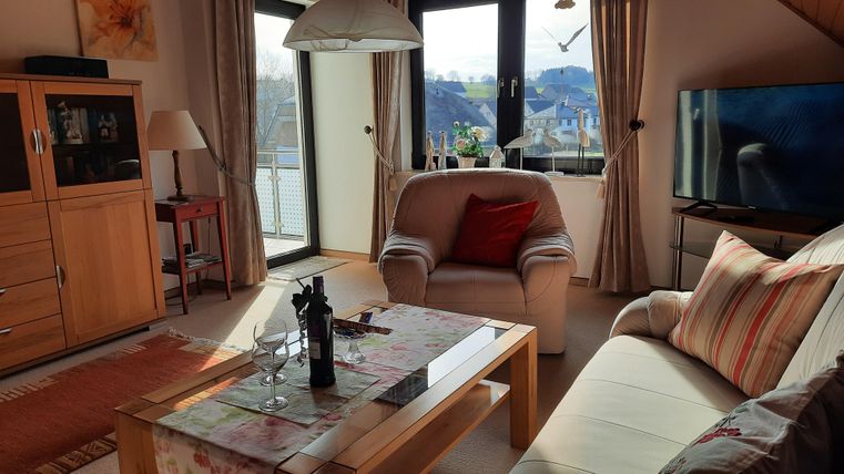 A cozy living room with a bright sofa and an armchair. Large windows provide a view of the landscape.