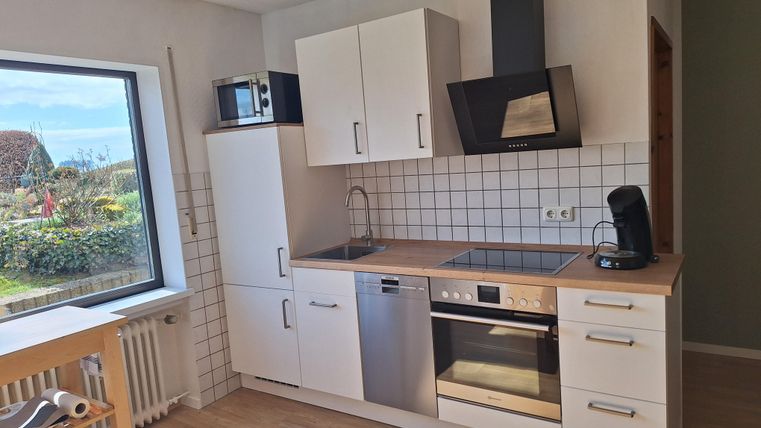 Een moderne keuken met witte kasten en een houten werkblad. Door het raam is een groene landschap zichtbaar.