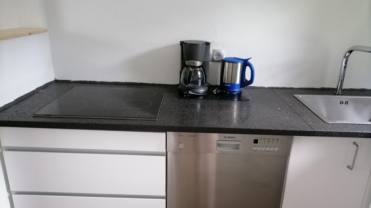Een moderne keuken met een zwarte werkruimte. Op het aanrecht staan een koffiezetapparaat, een waterkoker en een spoelbak.