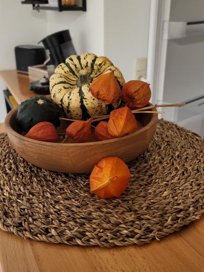 A bowl with colorful pumpkins and physalis on a woven placemat. The table has a modern cozy atmosphere.