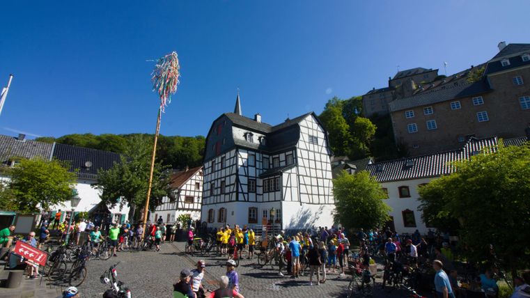 Een drukke plek met veel fietsers en een feestelijke sfeer. Op de achtergrond zijn historische gebouwen en bomen te zien.