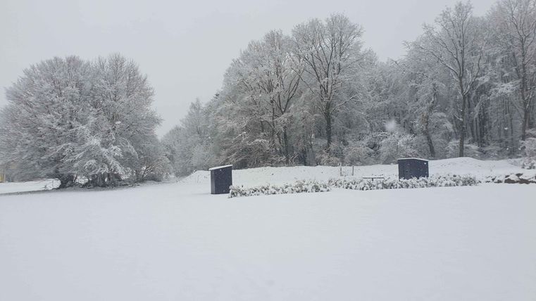 Eine winterliche Landschaft mit viel Schnee und schneebedeckten Bäumen. Im Hintergrund sind einige überfrorene Strukturen sichtbar.