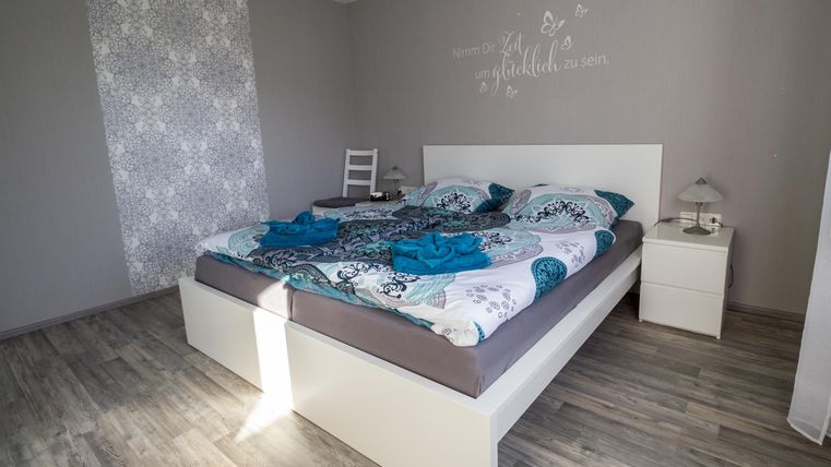 A cozy bedroom with a large bed and colorful bedding. The room has bright walls and a modern wooden floor.