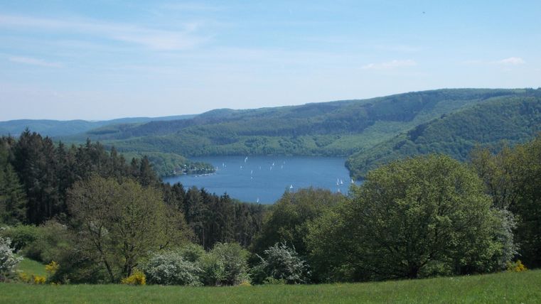 A picturesque lake surrounded by green hills and trees. The sky is clear and blue, ideal for outdoor activities.