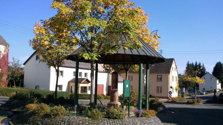 A beautiful pavilion surrounded by colorful autumn trees on a quiet street. In the background, there are old houses and a clear blue sky.