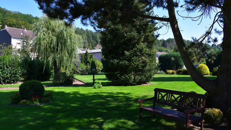 Ein schöner Garten mit üppigem Grün und schattenspendenden Bäumen. Eine Bank lädt zum Entspannen im Freien ein.