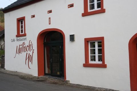 White building with red window frames and the inscription 'Müllisch's Hof'. Entrance door in dark wood.