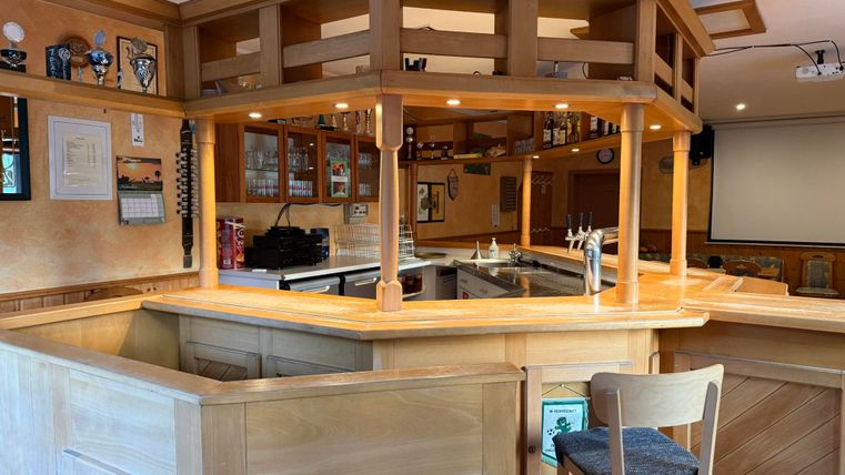 Eine gemütliche Holzbar mit Hockern und einer gut ausgestatteten Theke. Der Raum hat eine einladende Atmosphäre.