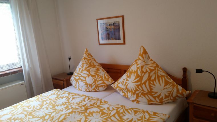 Ein gemütliches Schlafzimmer mit einem großen Bett und gelben Kissen. Die Wände sind hell und es gibt einen kleinen Nachttisch neben dem Bett.