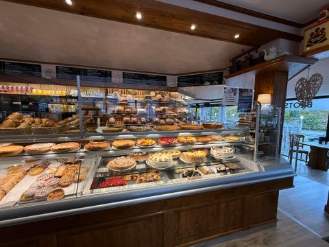 Eine gemütliche Bäckerei mit einer Auswahl an frisch gebackenem Brot und Kuchen. Im Vordergrund eine Tasse Kaffee und ein Teller mit einem Gebäck.