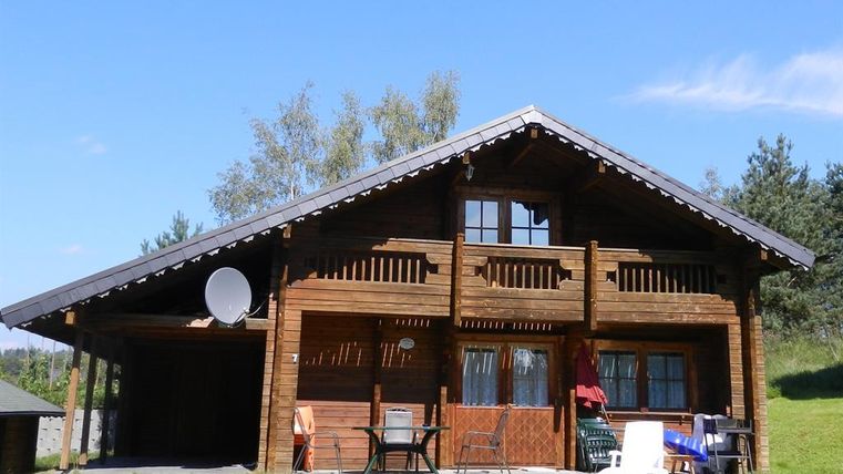 Ein gemütliches Holzhaus mit einem großen Balkon und großen Fenstern. Das Haus steht in einer grünen Umgebung, umgeben von Bäumen.