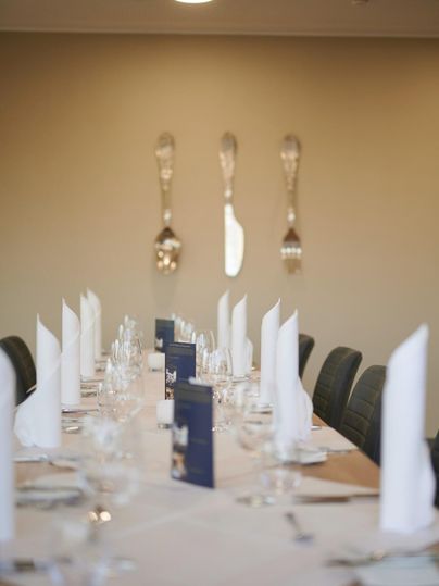 Ein elegant gedeckter Tisch mit weißen Servietten und Gläsern. Im Hintergrund sind dekorative Löffel an der Wand zu sehen.