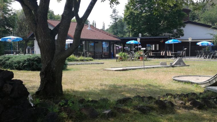 Ein ruhiger Garten mit einem Gebäude im Hintergrund. Es gibt Tische und Sonnenschirme für die Gäste.