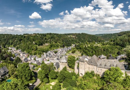 Panoramablick auf Monschau mit der Burg im Vordergrund, umgeben von gr&uuml;ner Landschaft und bewaldeten H&uuml;geln unter blauem Himmel mit Wolken., &copy; Eifel Tourismus GmbH, Dominik Ketz