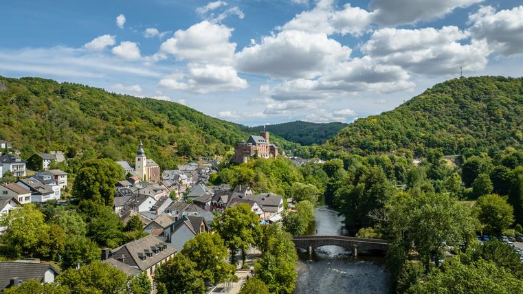 Ein malerisches Tal mit einer kleinen Stadt am Fluss. Grüne Hügel umgeben die sanfte Landschaft unter einem klaren Himmel.