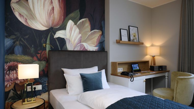 Ein modernes Hotelzimmer mit einer stilvollen Blumendekoration an der Wand. Es verfügt über ein bequemes Bett, einen Schreibtisch und eine angenehme Beleuchtung.