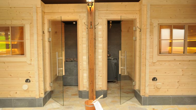 Zwei Duschen in einem Holzgebäude, jede mit transparenter Glastür. Der Boden ist mit natürlichen Steinen gestaltet.