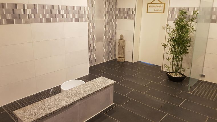 Ein modernes Spa mit eleganten Fliesen und einer ruhigen Atmosphäre. Eine dekorative Pflanze und eine Statue tragen zur Entspannung bei.