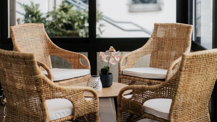 Ein gemütlicher Sitzbereich mit vier Rattanstühlen und einem kleinen Tisch. Auf dem Tisch stehen Blumen und ein Pflanzentopf.