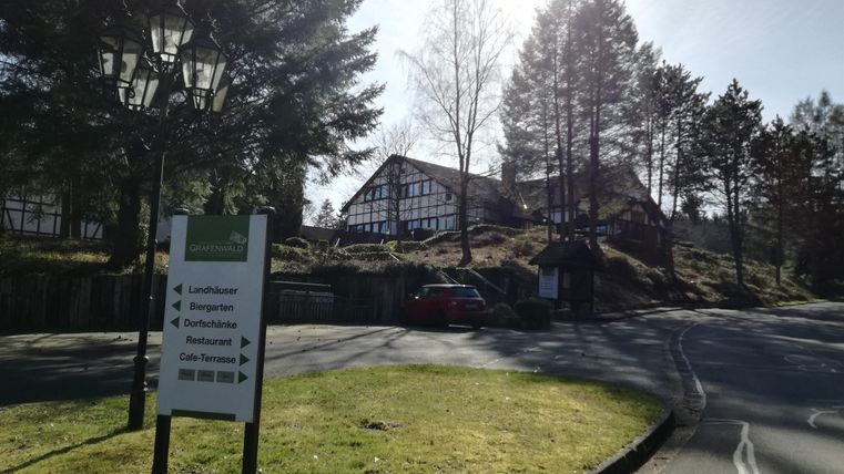 Een pittoresk gebouw te midden van bomen. De aangegeven oprit toont de weg naar verschillende voorzieningen.