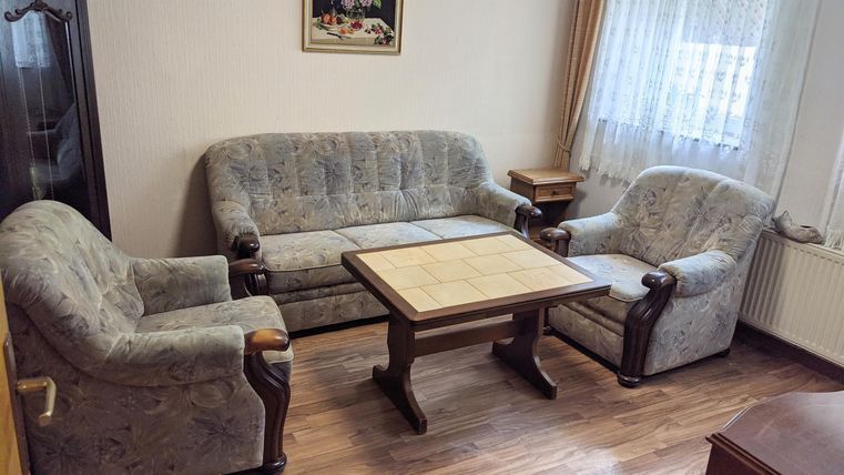 A cozy living room with a beige sofa and an armchair. A small wooden table is in the middle.