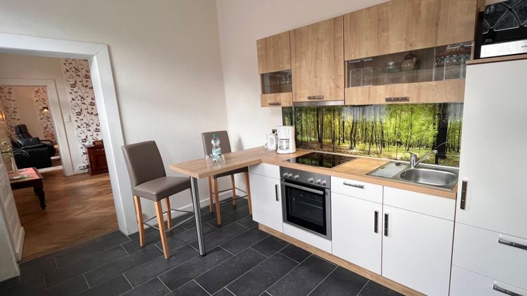 Eine moderne Küche mit Holz- und weißen Schränken. Im Hintergrund sind Bilder eines Waldes sichtbar.