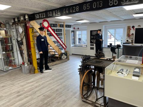 <p>man blickt in ein helles Zimmer, das vollgestellt ist mit alten Eisenbahngegenständen. In der Mitte stehen zwei Schaufensterpuppen in  Eisenbahneruniformen.An den Wänden hängen alte Schilder mit Zugnummern. Als Geländer an der Treppe dient ein Eisenbahnsignal. In mehreren Vitrinen sind Schriftstücke und Werkzeuge ausgestellt.</p>