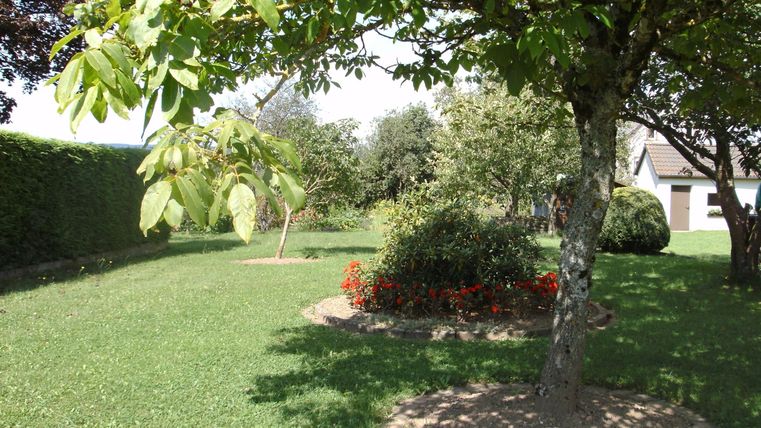 Ein schöner Garten mit grünem Gras und mehreren Bäumen. Im Vordergrund sind bunte Blumenbeete zu sehen.