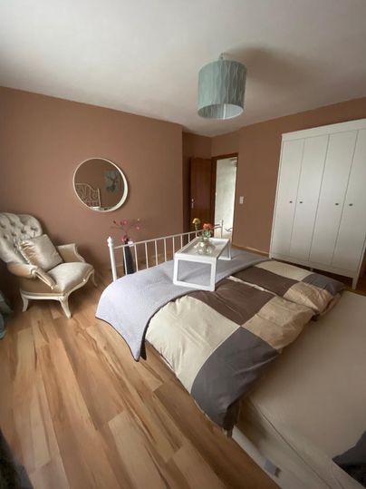 Ein gemütliches Schlafzimmer mit einem Bett, das eine gestreifte Bettdecke hat. Ein bequemer Sessel und ein runder Spiegel ergänzen den Raum.