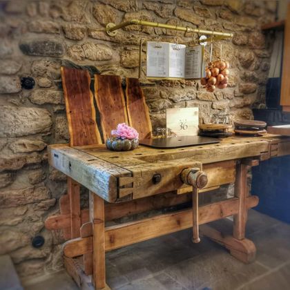 Ein rustikaler Holztisch mit einem Schleifwerkzeug aus Holz und Kochbüchern. An der Wand hängen Zwiebeln und es gibt eine kleine Blumendekoration.