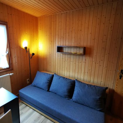 Een gezellige kamer met houten wanden. Een blauwe bank met kussens en een vloerlamp creëren een uitnodigende sfeer.